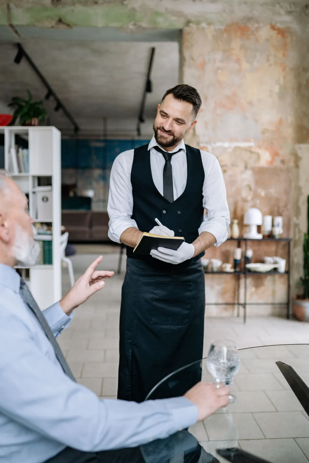 A waiter taking an order at the table while the guest looks up from the menu